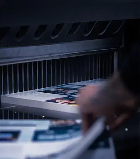 Service-home-1 A person’s hand removing freshly printed sheets from a high-tech industrial paper cutting machine in a printing workshop.
