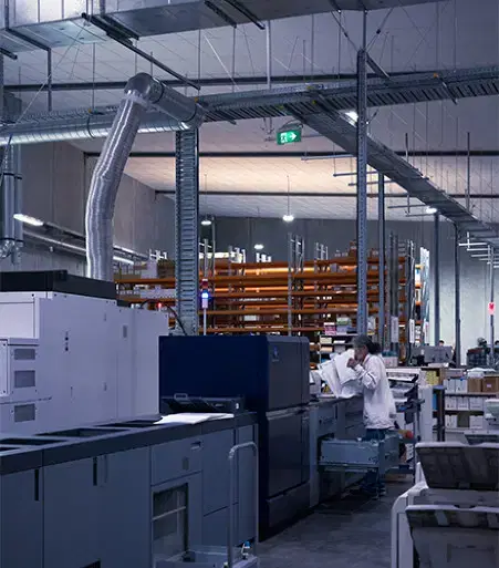Service-home-3 A man in a white shirt inspecting printouts on a large commercial printing machine inside an industrial printing facility.