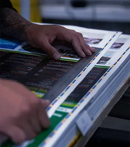 Service-home-8 Close-up of hands using a ruler to measure or align printed sheets in a professional printing environment.
