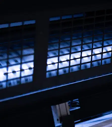 Services-IT Close-up of the illuminated inside of a printing machine showing metal parts and a glowing blue light in a dark setting.